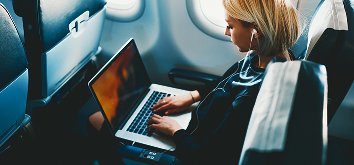 Mulher sentada na poltrona do avião com utilizando laptop e fones de ouvido
